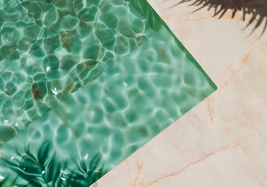 Top view of luxury swimming pool with palm shadow and marble floor. Summer background for tropical holiday vacation. Modern hotel villa, poolside water from above. Product placement showroom design.