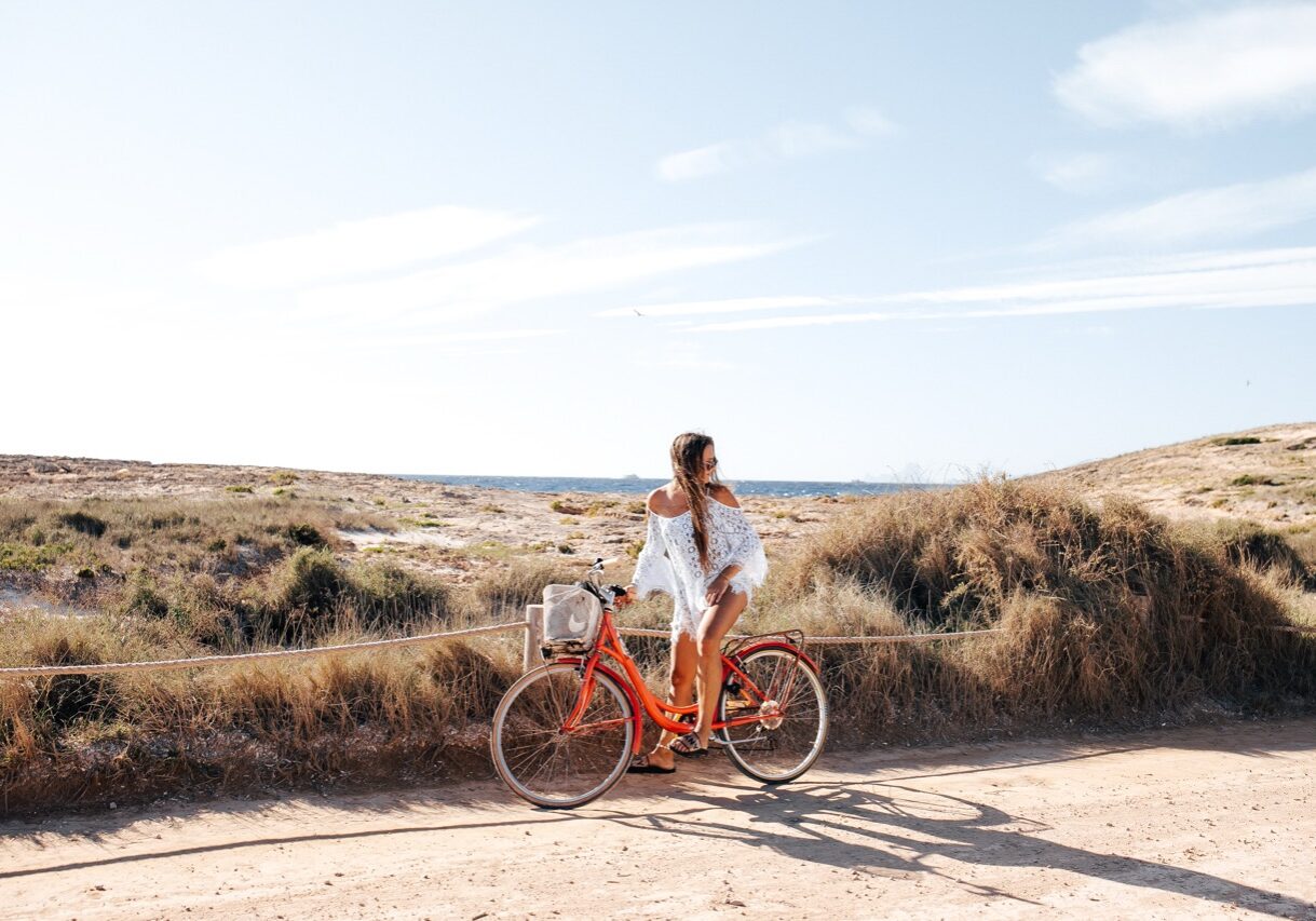 Formentera, Ibiza/Spain - September 23, 2019: Young woman positive charming girl on red vintage bike waiting for friends looking back. Near the sea.