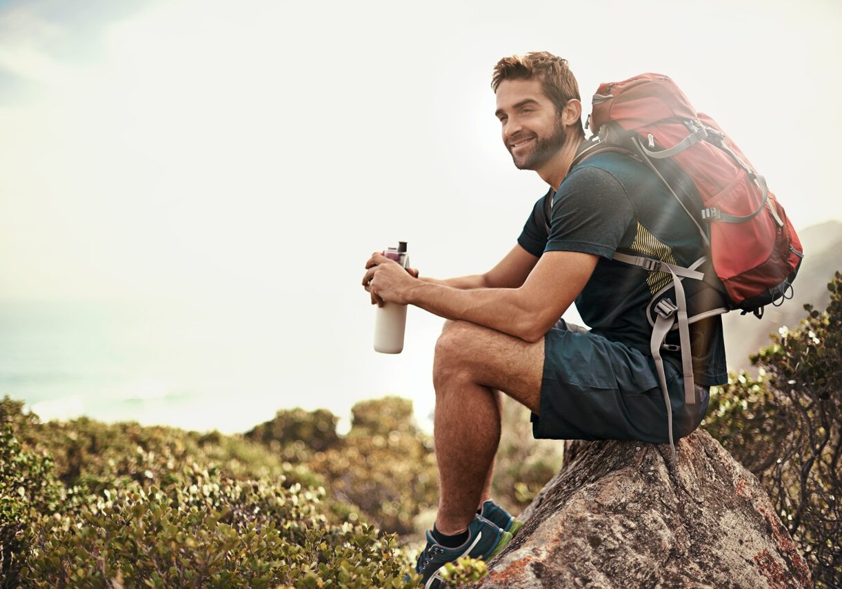 Shot of a young man taking a water break while out hiking.