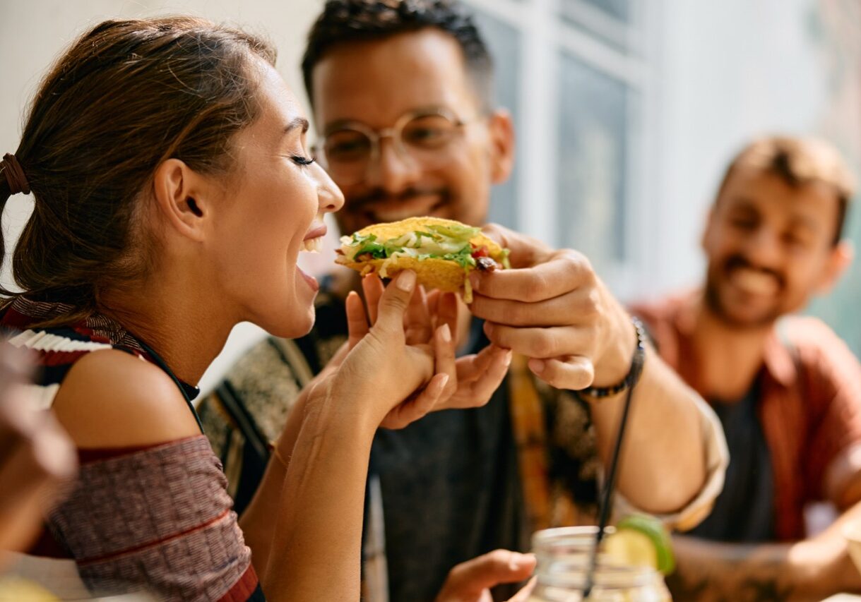 Happy couple sharing taco while eating in Mexican restaurant..